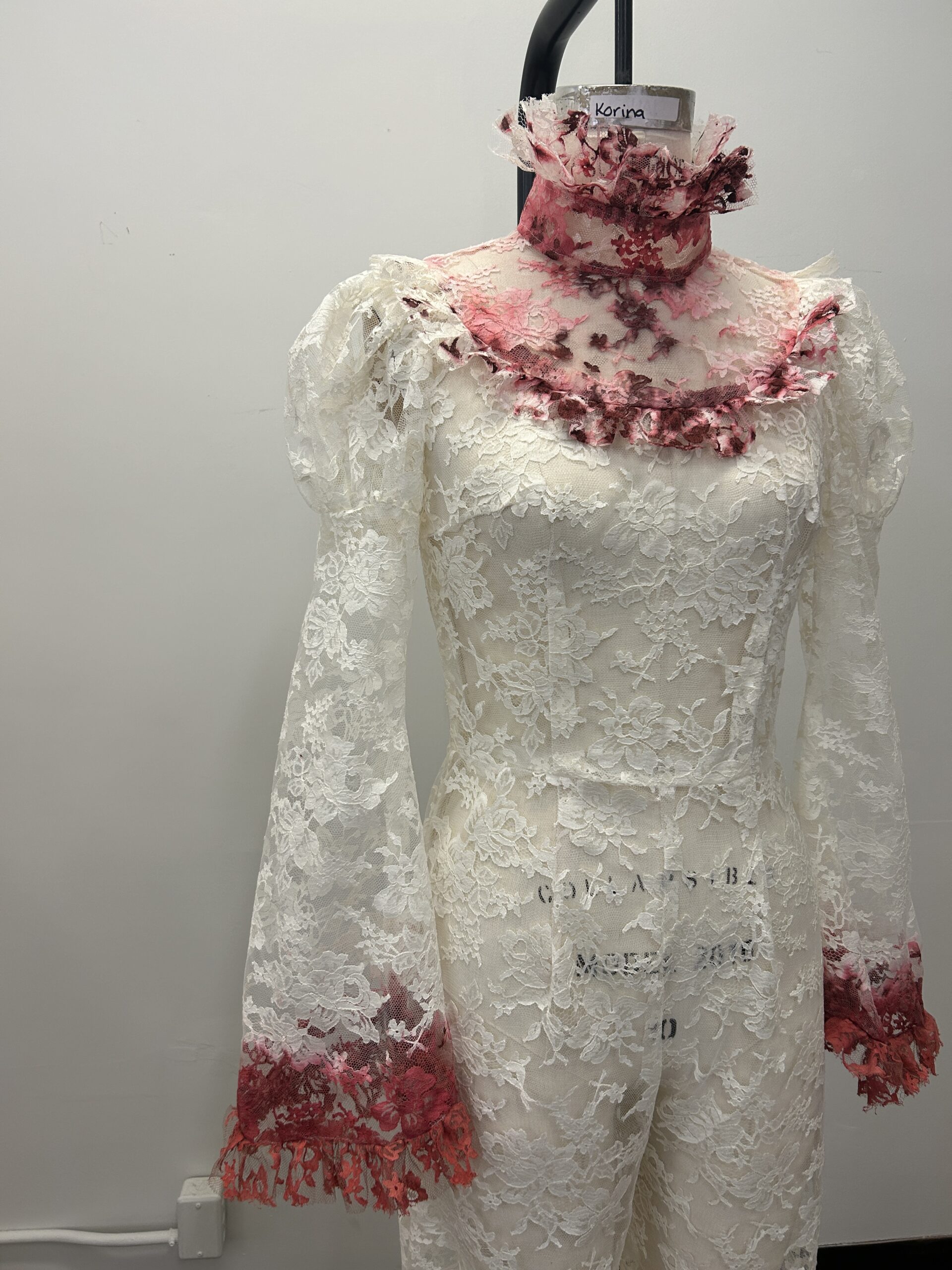 A close-up of hand dyed fake blood stains on the sleeves and bodice of an ivory sheer lace jumpsuit.